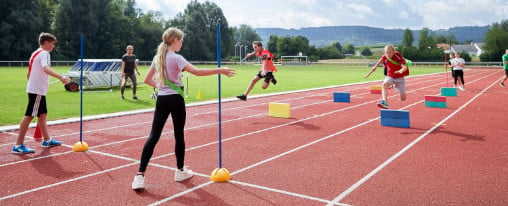 Schülerinnen und Schüler auf der Kunststoffbahn mit Schulsportartikeln